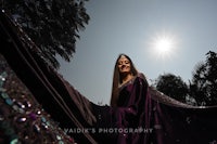 a woman in a purple sari posing with the sun behind her